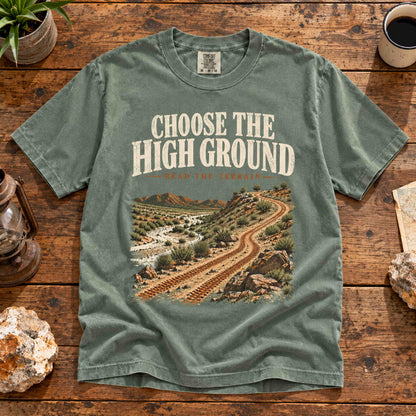 Overhead view of the Moss Choose the High Ground graphic tee on a wooden table with desert trail artwork.