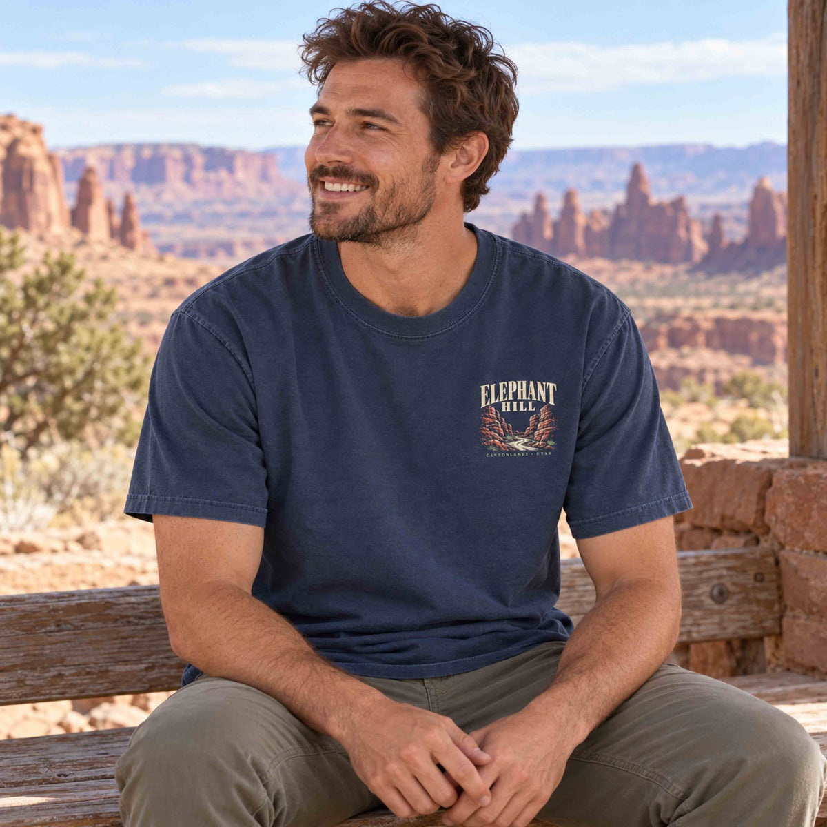 Seated man wearing a Navy Elephant Hill tee with the small left-chest canyon and trail graphic visible.
