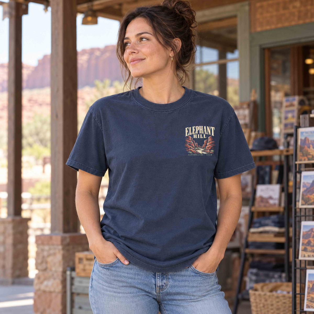 Woman wearing a Navy Elephant Hill tee with a small left-chest canyon graphic outside a desert shop.