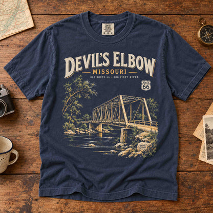 Navy Devil's Elbow Missouri Route 66 T-shirt laid flat on wood, showing the bridge and Big Piney River artwork.