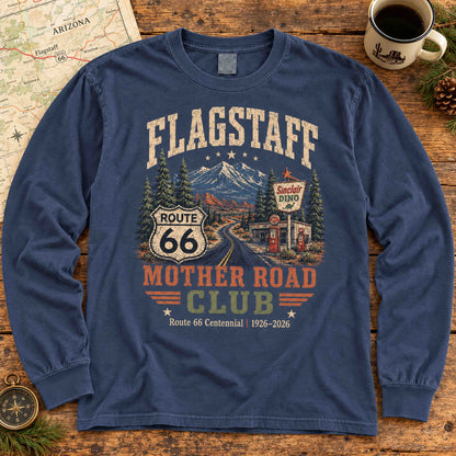 Navy Flagstaff Route 66 long sleeve tee laid flat beside an Arizona map and coffee, showing mountain, pine tree and roadside gas station artwork.