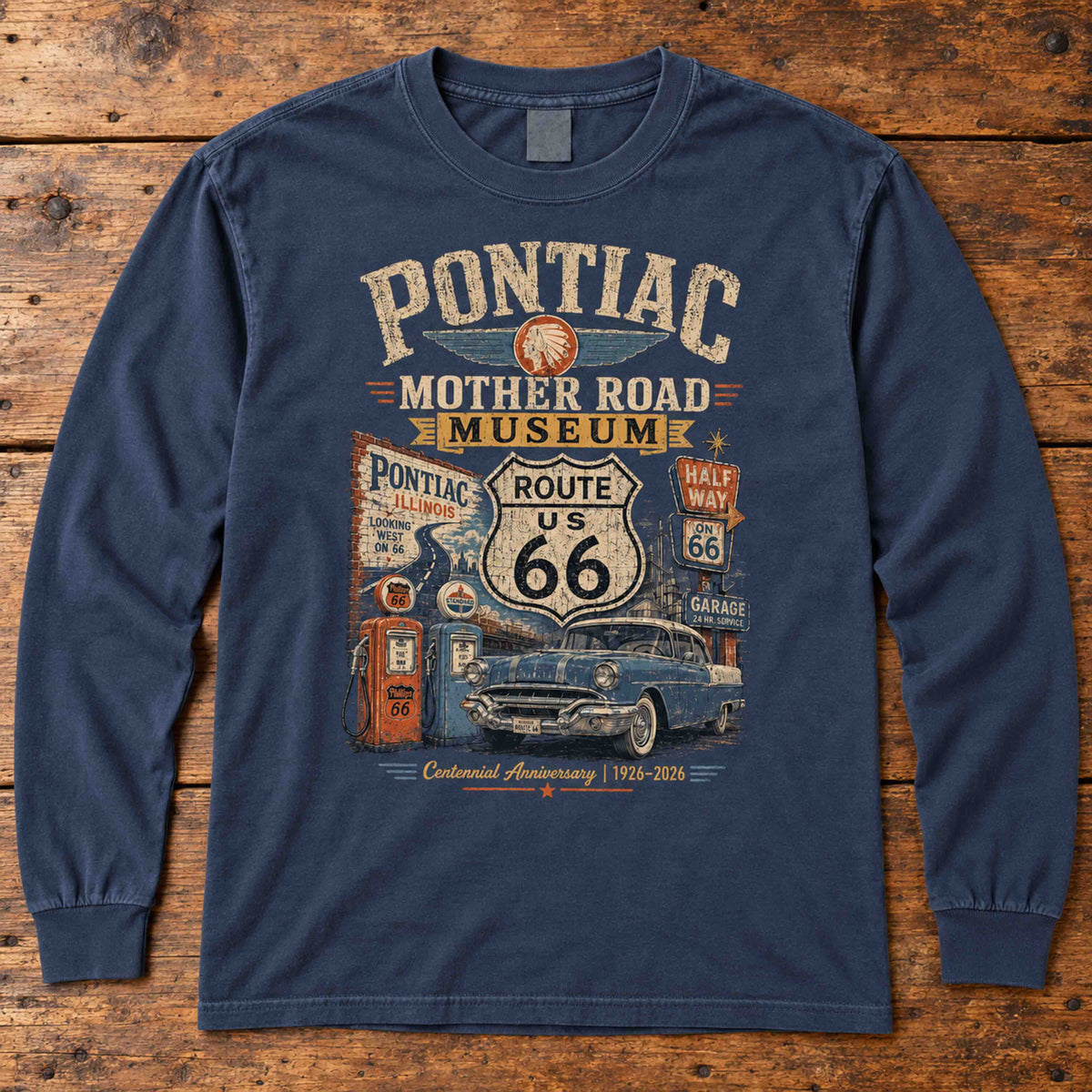 Navy Pontiac Illinois Route 66 long sleeve tee laid flat on wood, showing classic car, gas pumps and centennial artwork.