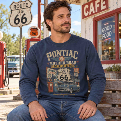 Man seated on a bench wearing a Navy Pontiac Illinois Route 66 long sleeve graphic tee outside a cafe.