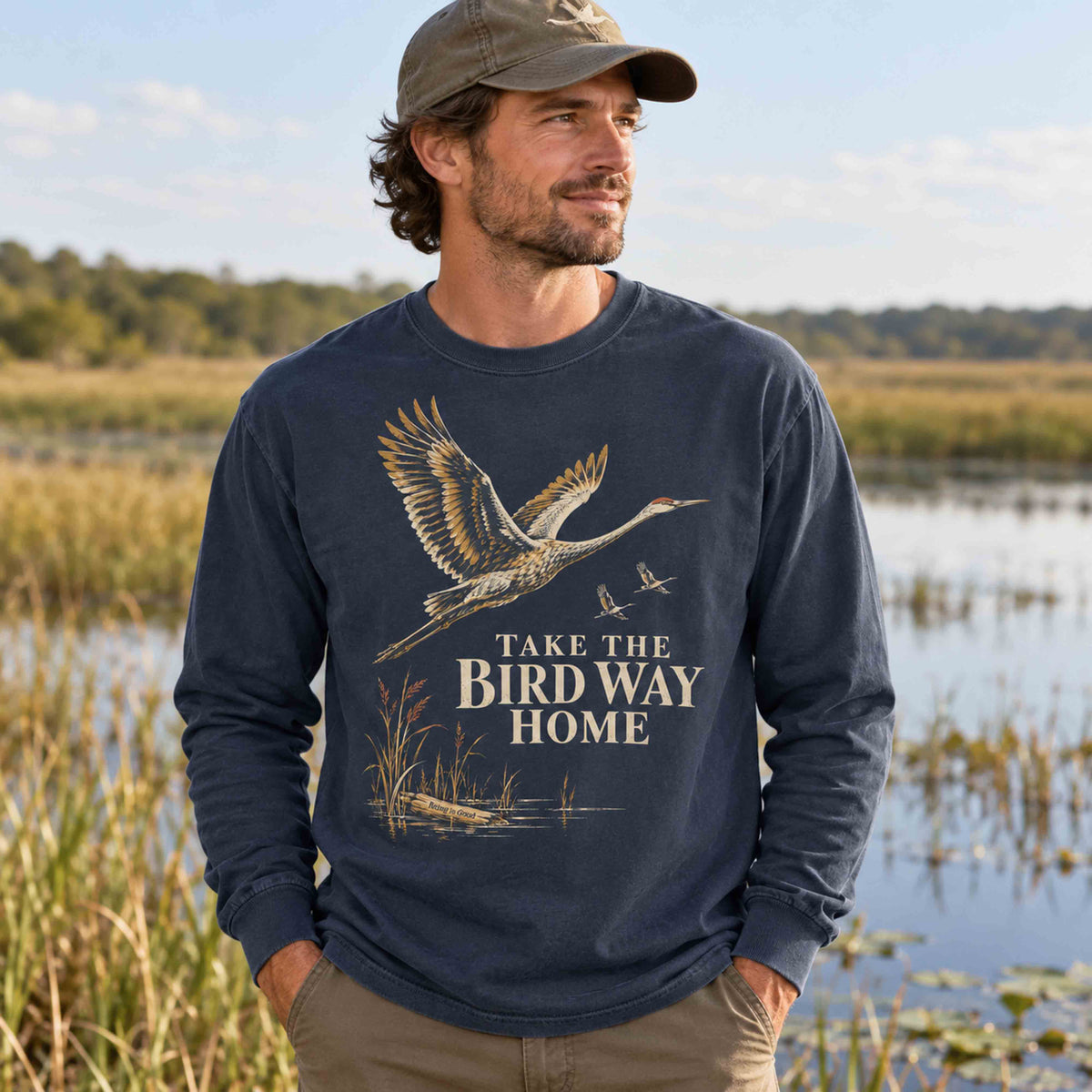 Man wearing the Navy sandhill crane long sleeve shirt beside a wetland.