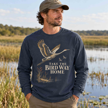 Man wearing the Navy sandhill crane long sleeve shirt beside a wetland.