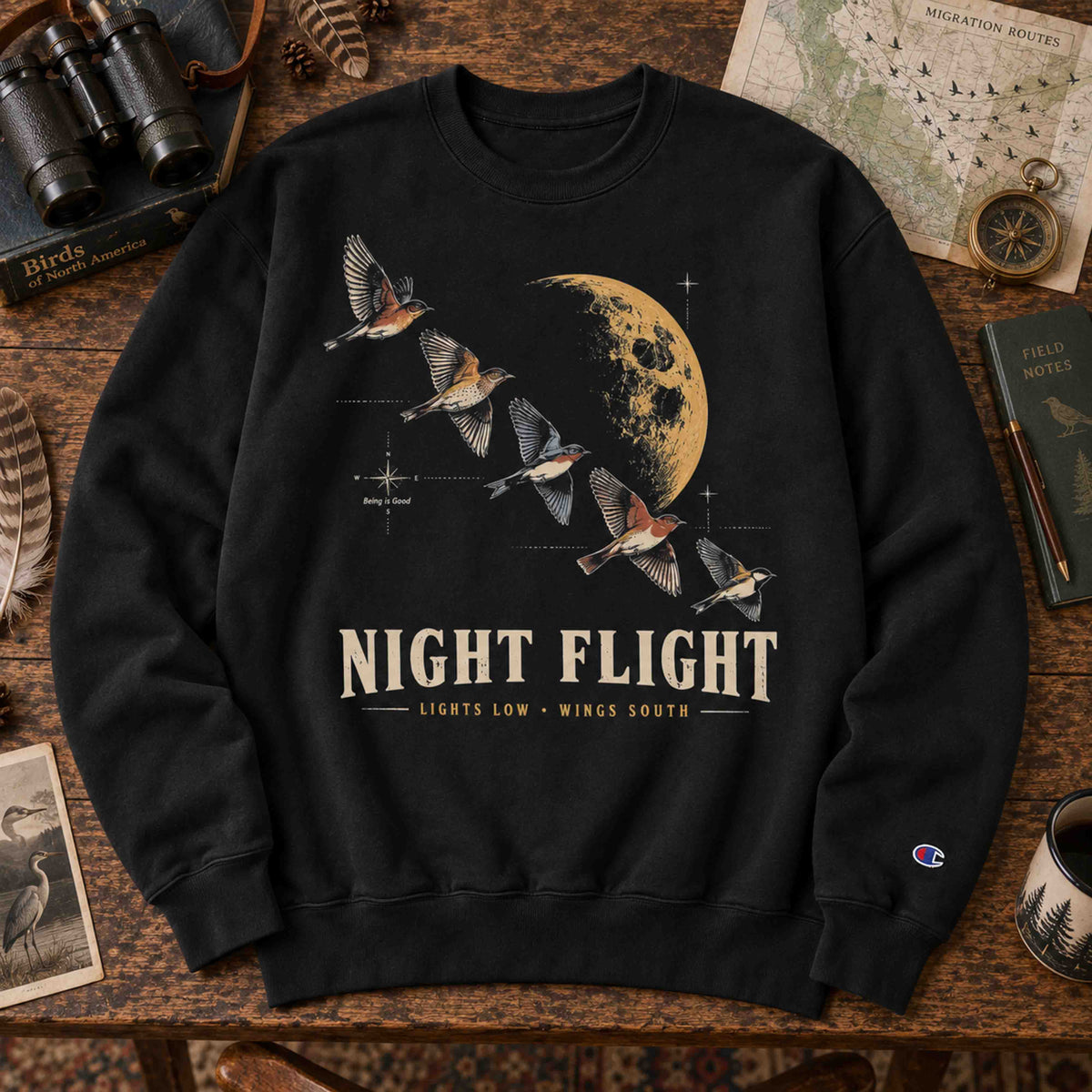 Black and Navy Night Flight Bird Migration Champion sweatshirts shown in a birdwatching flat lay