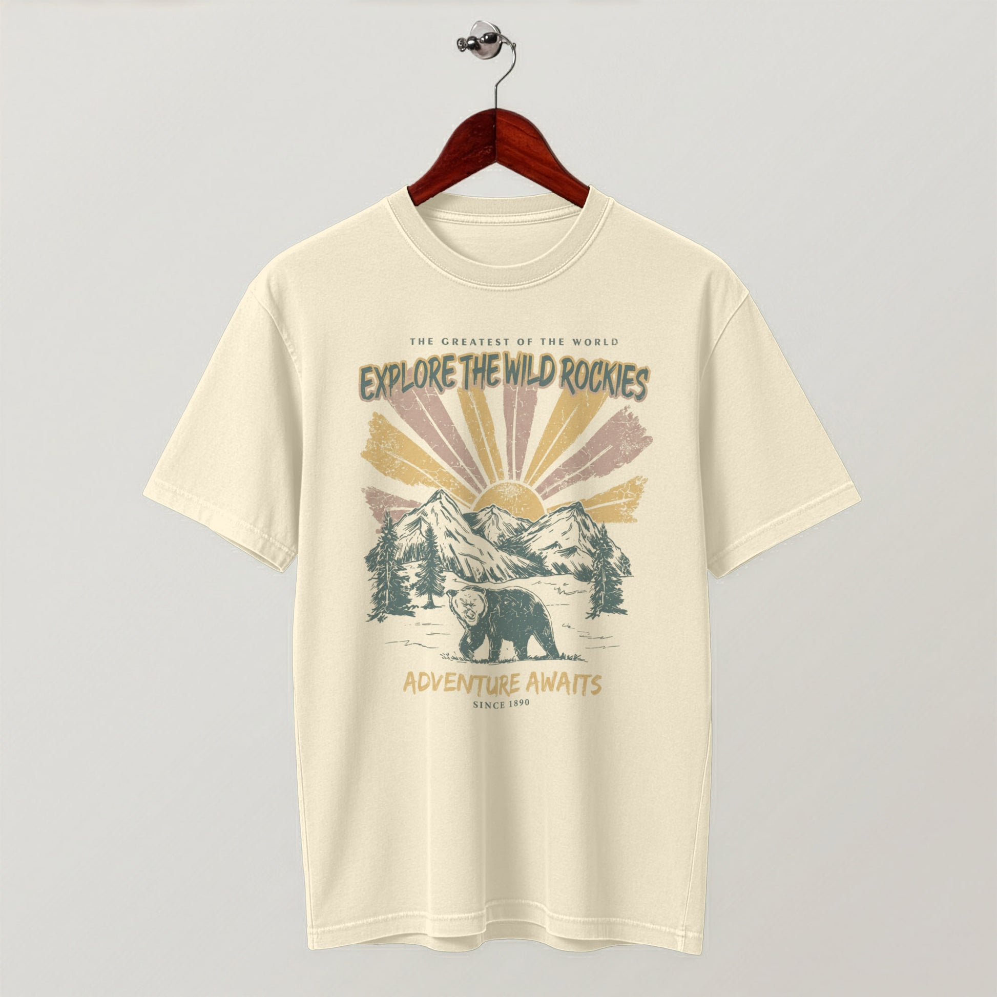 Cream-colored "Explore the Wild Rockies" graphic t-shirt hanging flat on a wooden hanger.