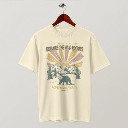Cream-colored "Explore the Wild Rockies" graphic t-shirt hanging flat on a wooden hanger.