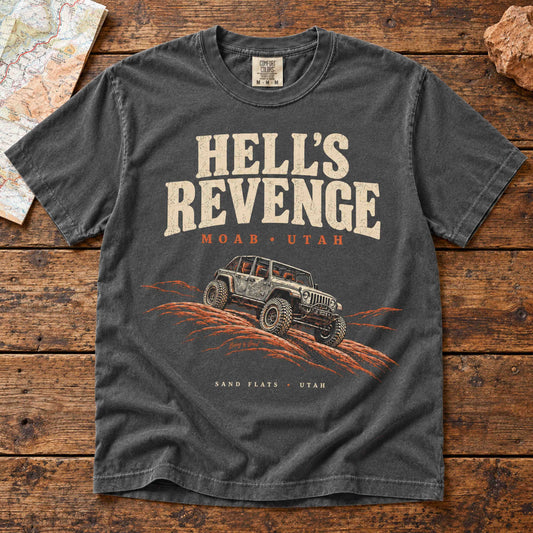 Pepper Hell’s Revenge graphic t-shirt laid flat on a vintage wooden table, featuring an off-road vehicle on orange slickrock.
