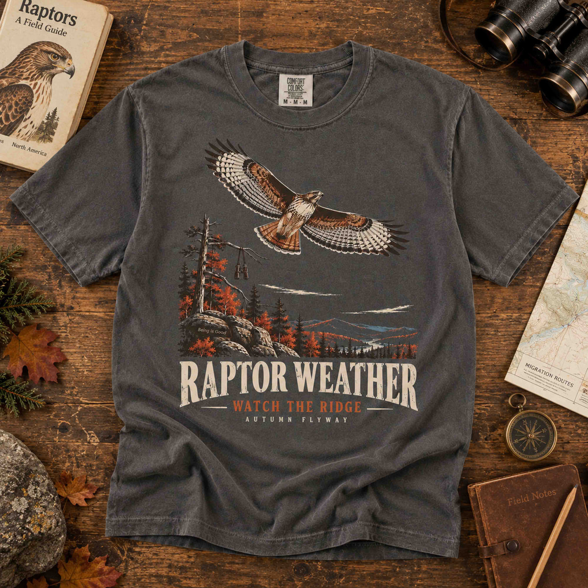 Navy and Pepper Raptor Weather Autumn Flyway graphic tees displayed in a birdwatching field station flat lay
