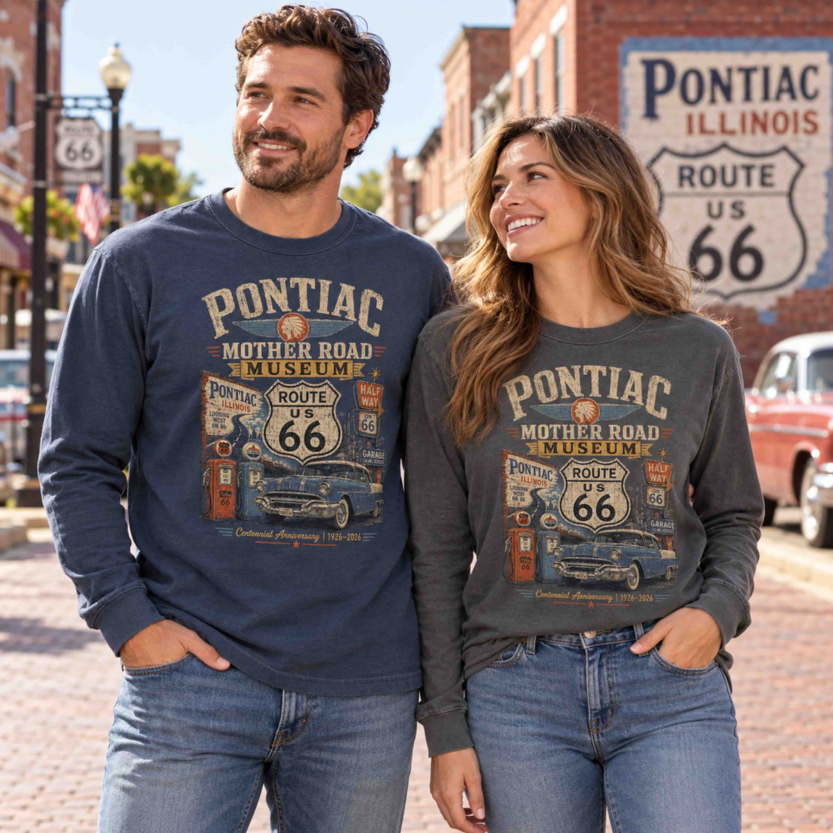 Man in Navy and woman in Pepper wearing Pontiac Illinois Route 66 long sleeve graphic tees with classic car and gas pump artwork.