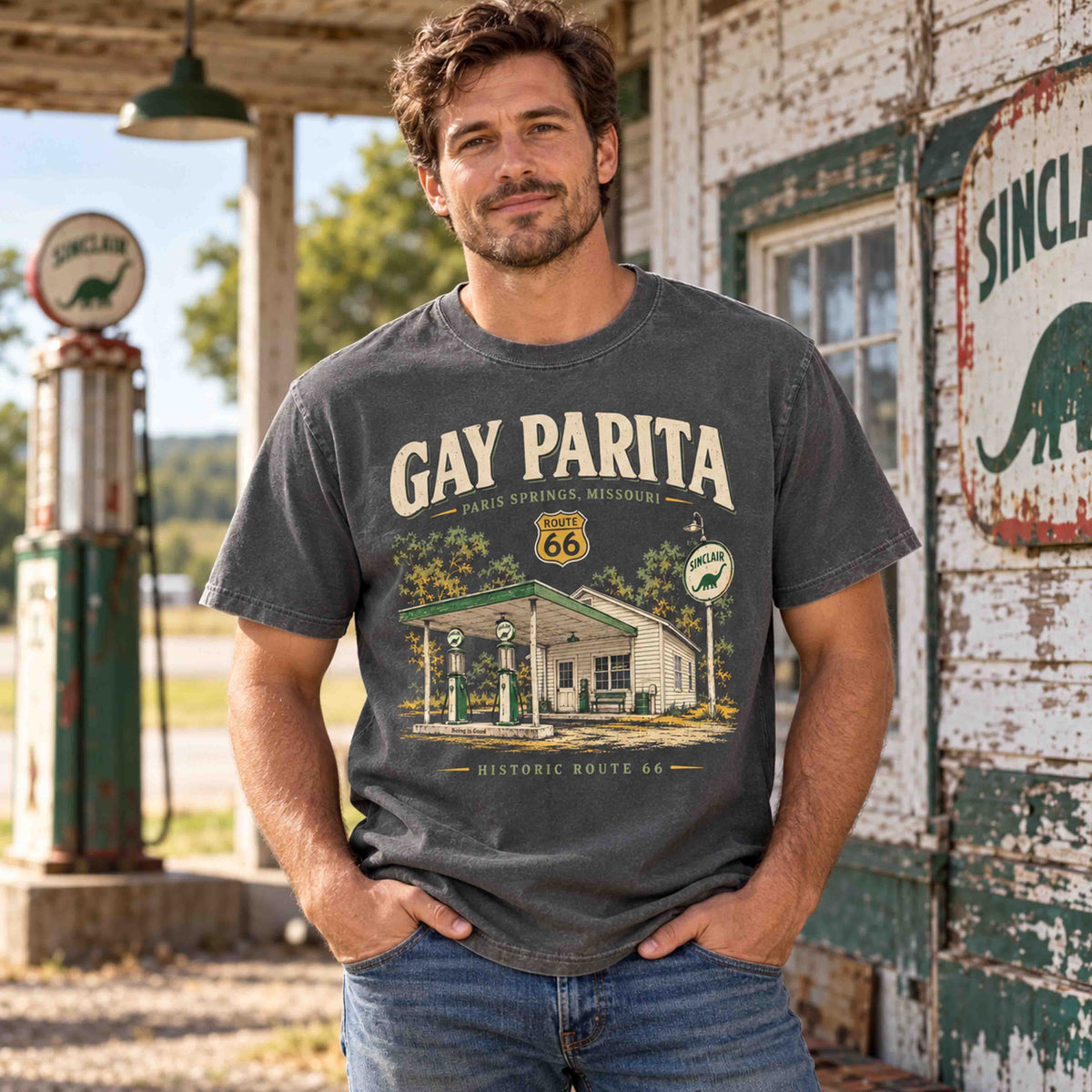 Man wearing a Pepper Gay Parita Paris Springs Route 66 graphic T-shirt near vintage gas pumps and station signage.