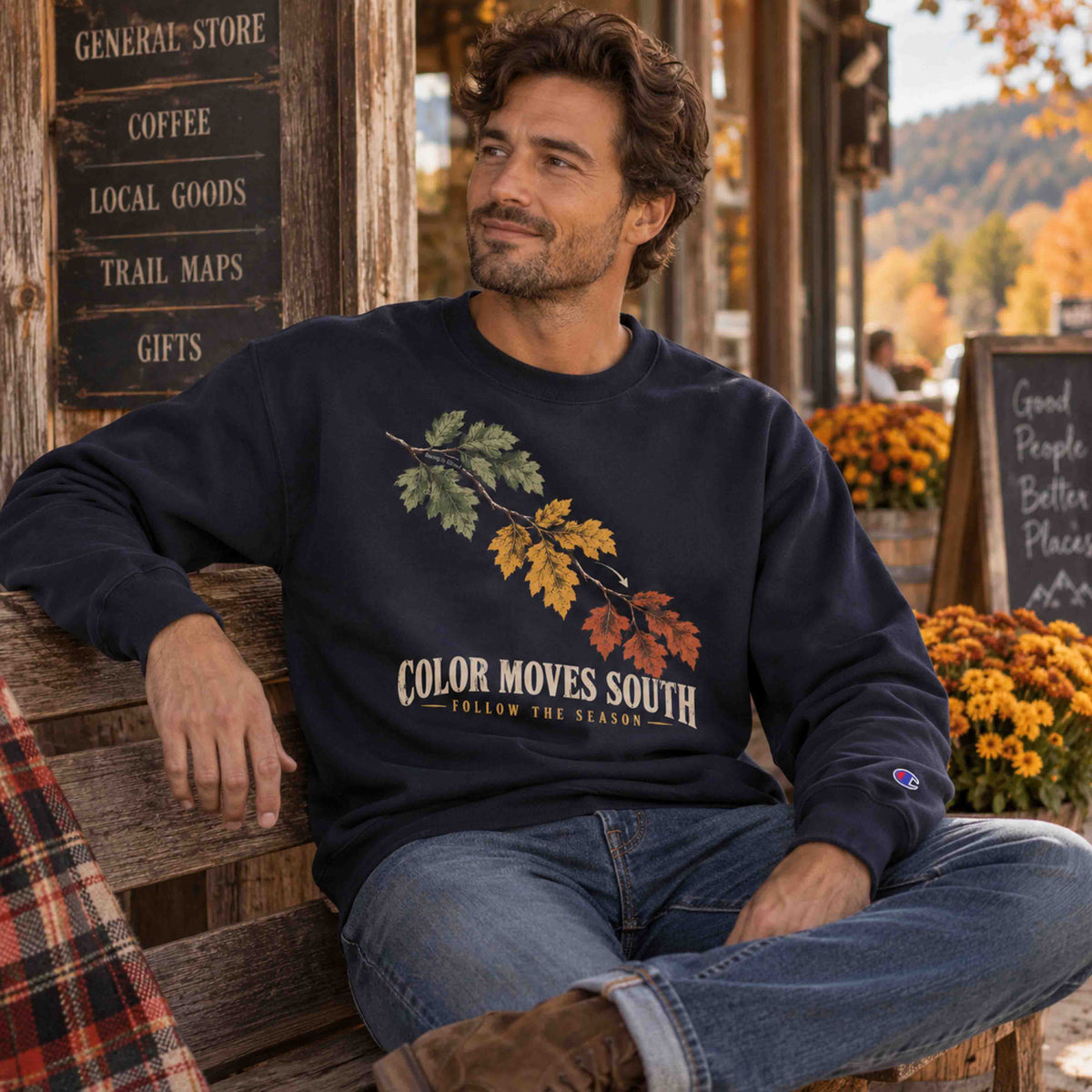 Man seated outside a rustic general store wearing a Navy Being is Good Color Moves South sweatshirt.