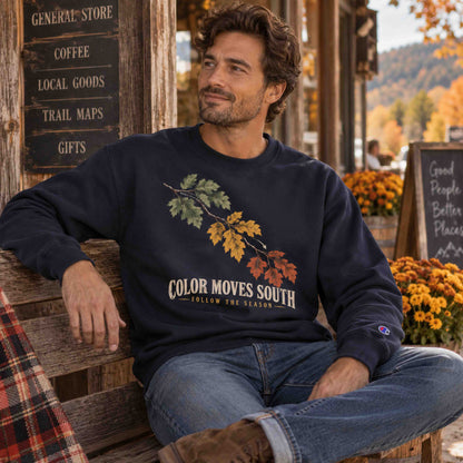 Man seated outside a rustic general store wearing a Navy Being is Good Color Moves South sweatshirt.
