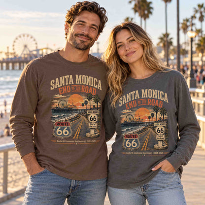 Man in Espresso and woman in Pepper wearing Santa Monica Route 66 long sleeve tees beside the beach, with the pier and Ferris wheel behind them.
