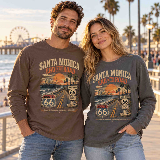 Man in Espresso and woman in Pepper wearing Santa Monica Route 66 long sleeve tees beside the beach, with the pier and Ferris wheel behind them.