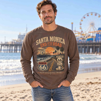 Man wearing an Espresso Santa Monica Route 66 long sleeve graphic tee on the beach, with the pier and Ferris wheel in the background.