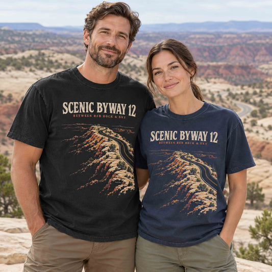 Couple wearing black and navy Scenic Byway 12 graphic T-shirts with winding red rock highway artwork at a desert overlook.