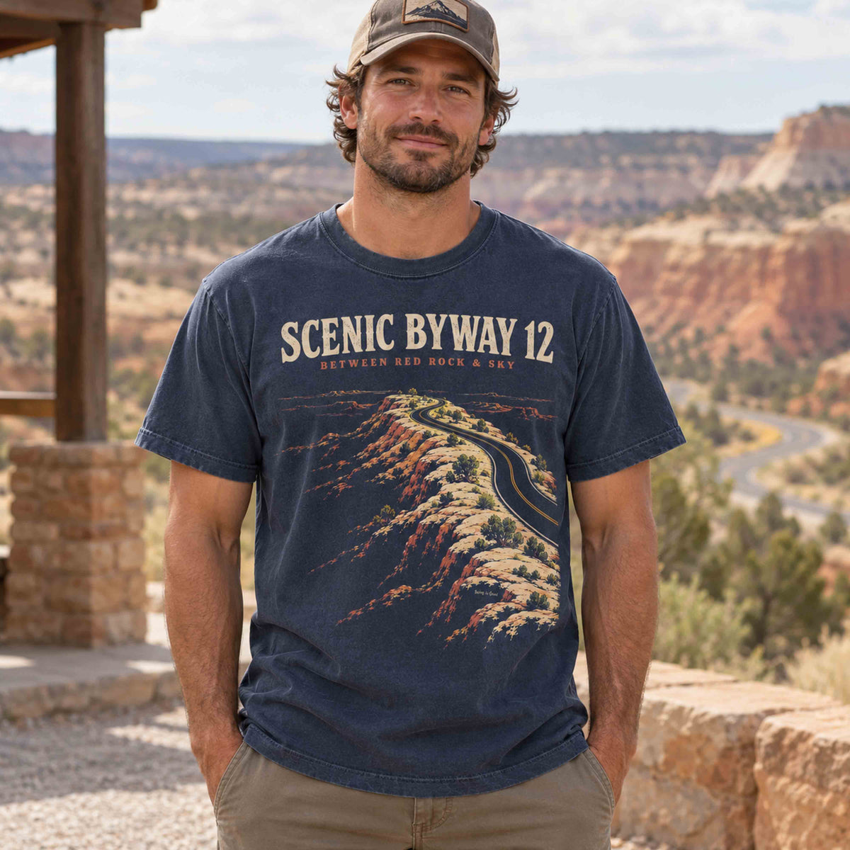 Man wearing a navy Scenic Byway 12 graphic T-shirt at a roadside overlook with red rock scenery.