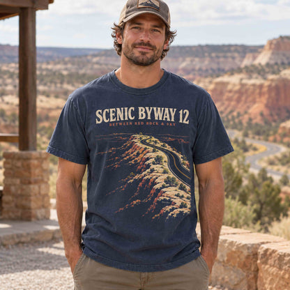 Man wearing a navy Scenic Byway 12 graphic T-shirt at a roadside overlook with red rock scenery.