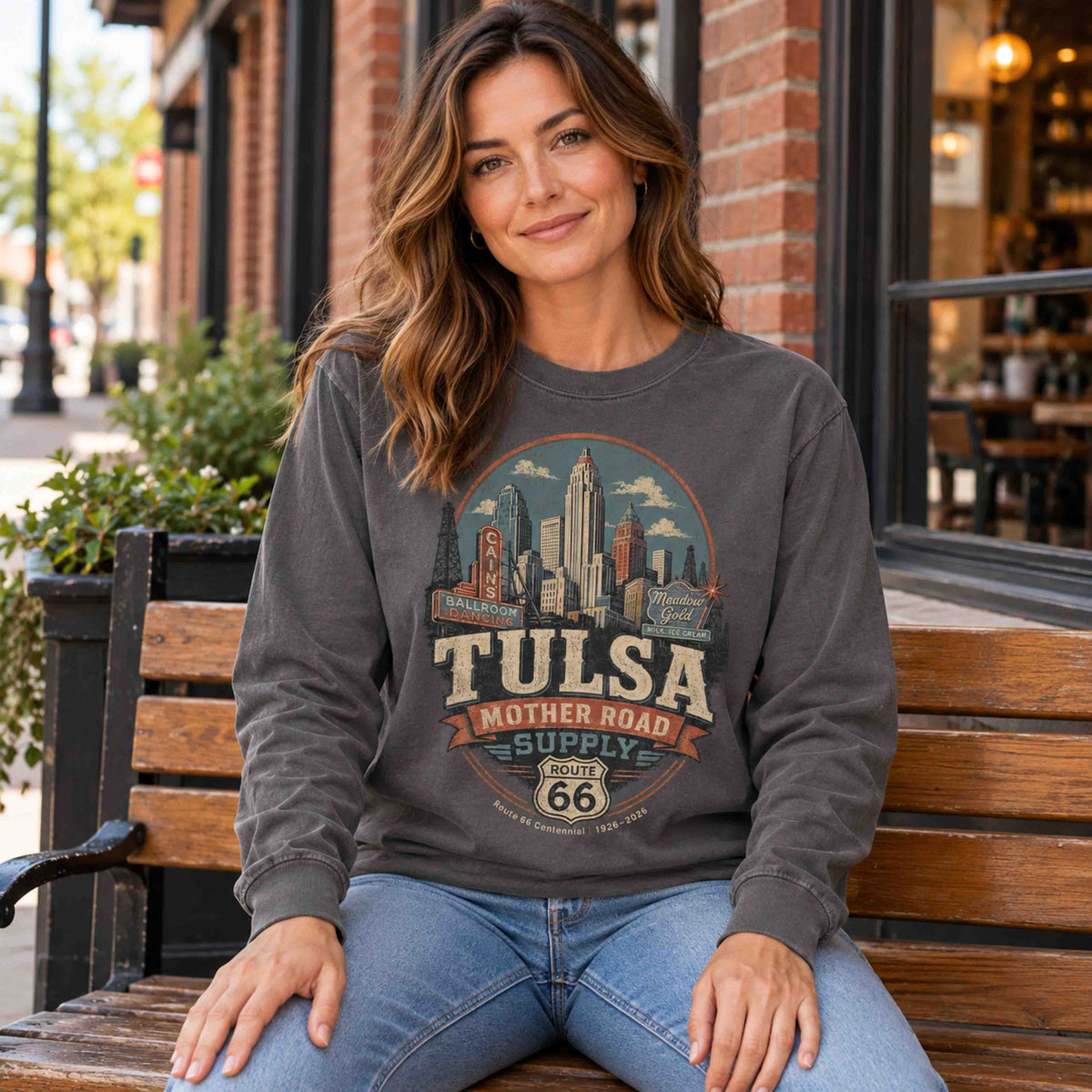 Woman seated on a wooden bench wearing a Pepper Tulsa Oklahoma Route 66 long sleeve graphic tee.