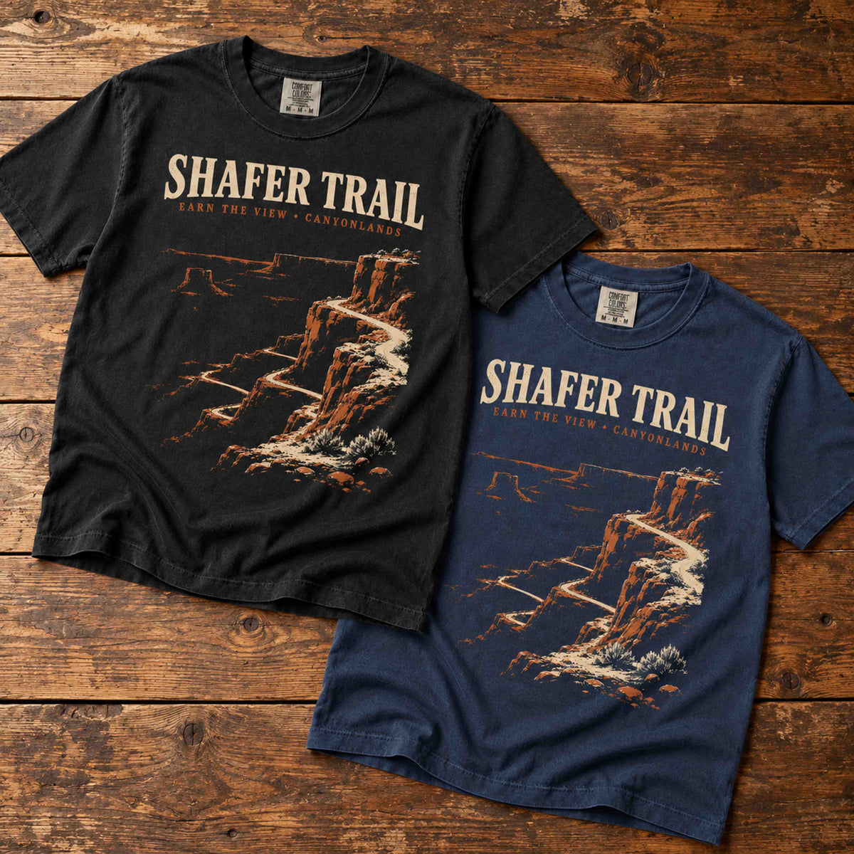Black and Navy Shafer Trail Canyonlands T-shirts arranged diagonally on vintage wood.