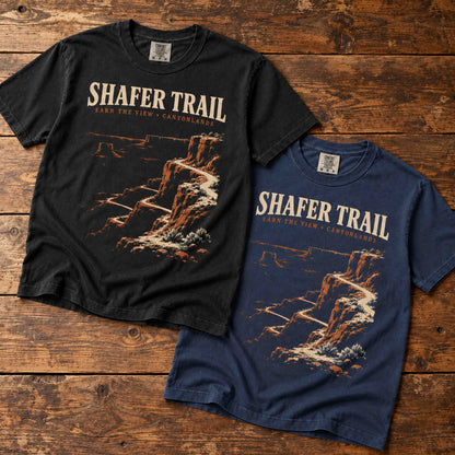 Black and Navy Shafer Trail Canyonlands T-shirts arranged diagonally on vintage wood.