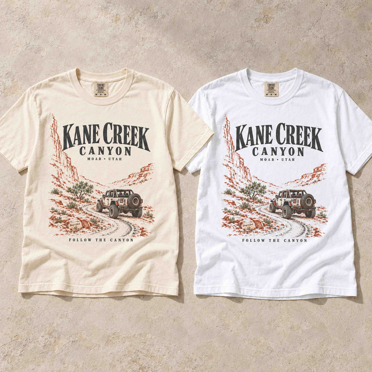 Ivory and White Kane Creek Canyon graphic tees laid flat side by side.