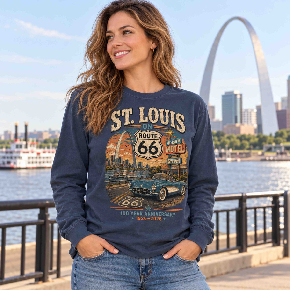 Woman wearing a Navy St. Louis Route 66 long sleeve graphic tee beside a riverfront railing and the Gateway Arch.