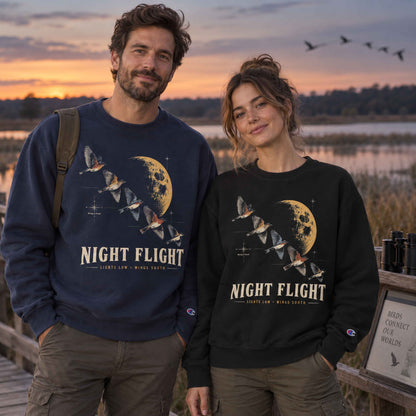 Couple wearing Navy and Black Champion Night Flight Bird Migration graphic sweatshirts at a wetland boardwalk at sunset
