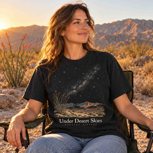 Woman seated in a camping chair wearing a Black Under Desert Skies Borrego Springs graphic T-shirt at sunset.