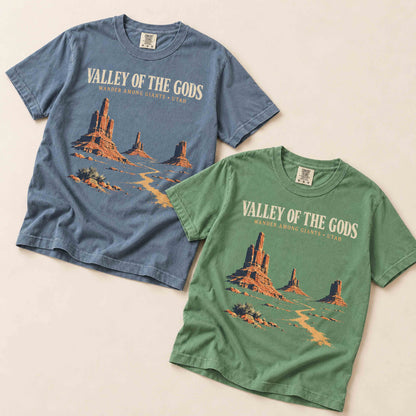 Blue Jean and Light Green Valley of the Gods Utah graphic T-shirts arranged diagonally on a cream background.