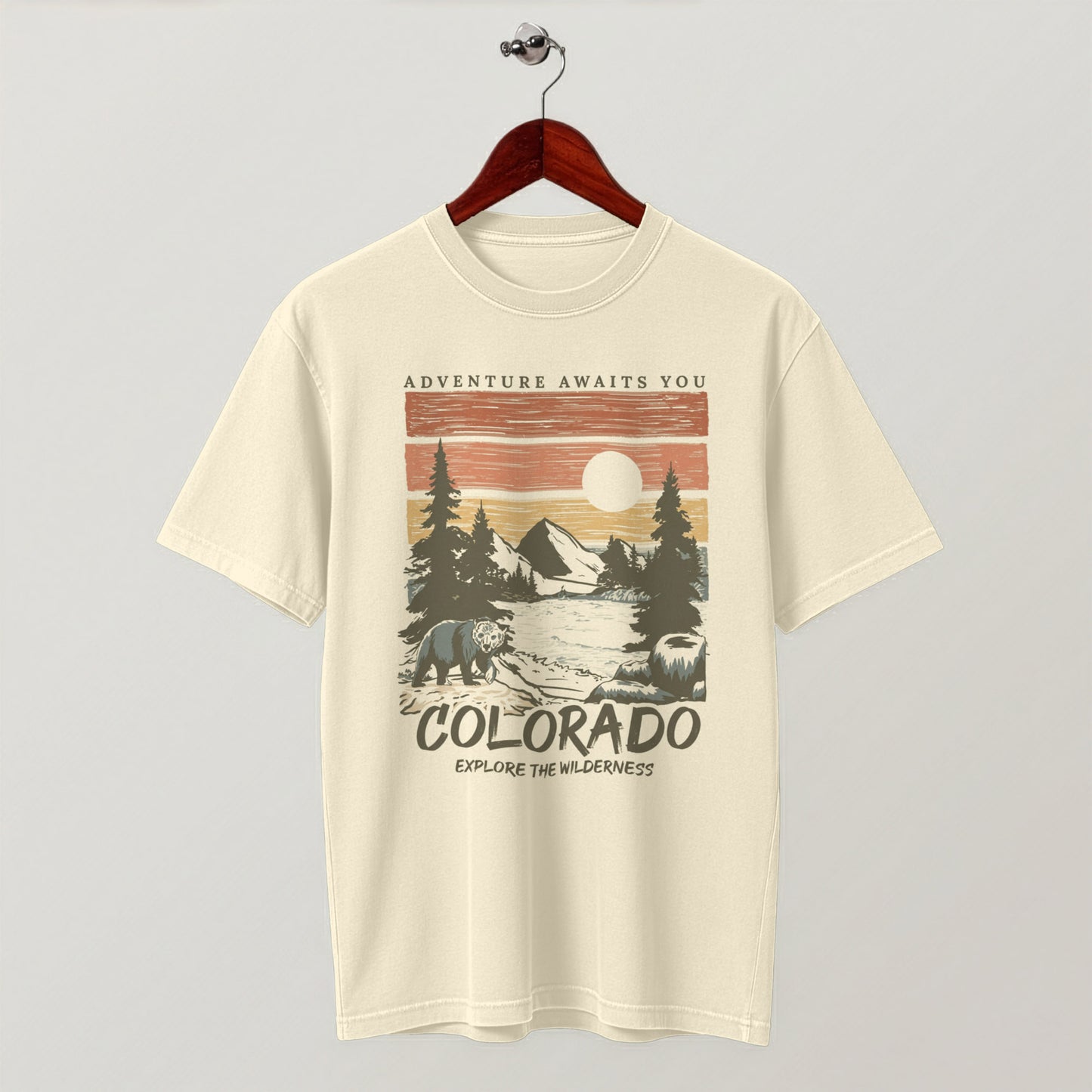 Cream-colored Colorado wilderness graphic t-shirt hanging flat on a wooden hanger.