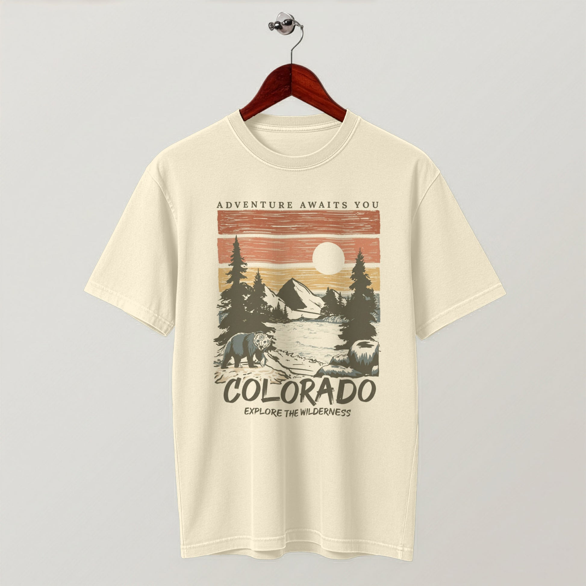 Cream-colored Colorado wilderness graphic t-shirt hanging flat on a wooden hanger.