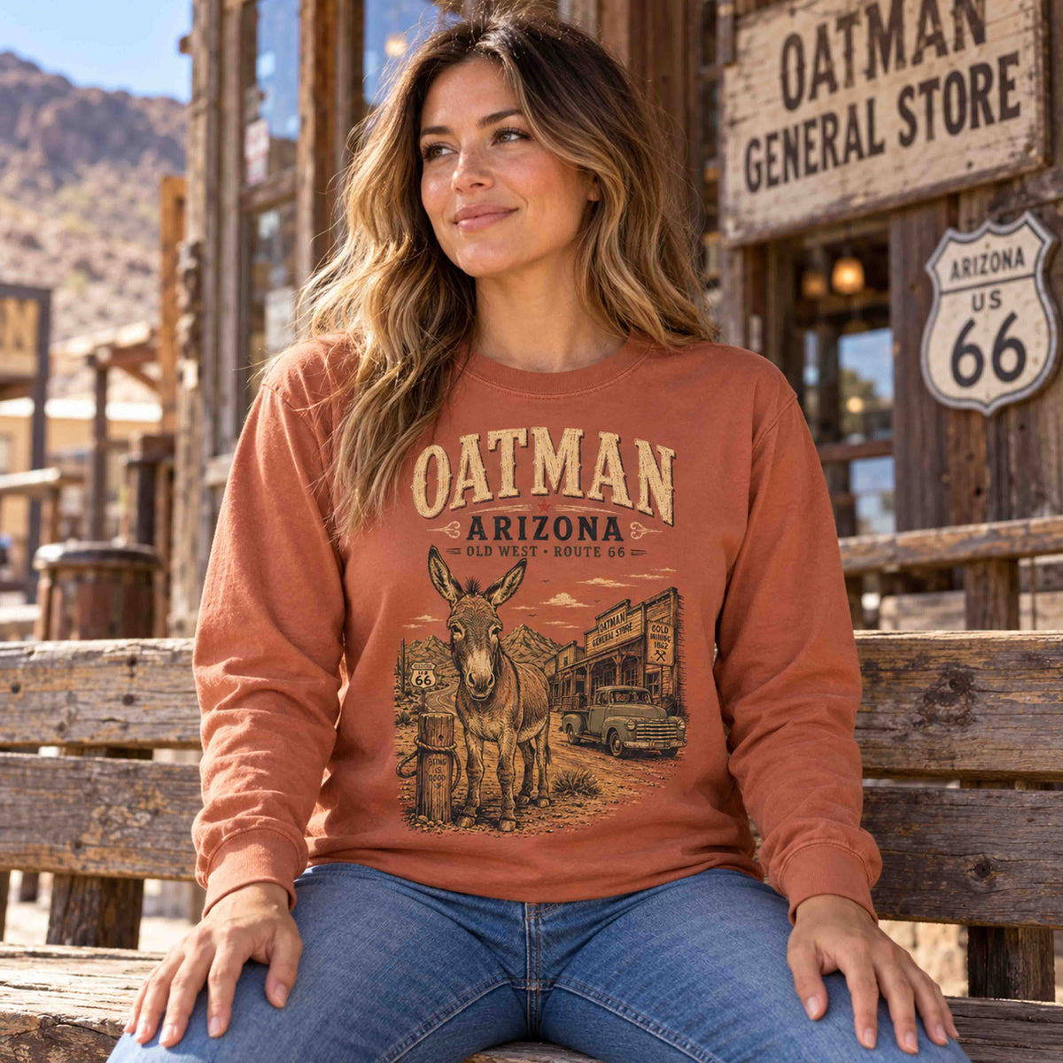 Woman seated on a wooden bench wearing a Yam Oatman Arizona Route 66 burro long sleeve tee.