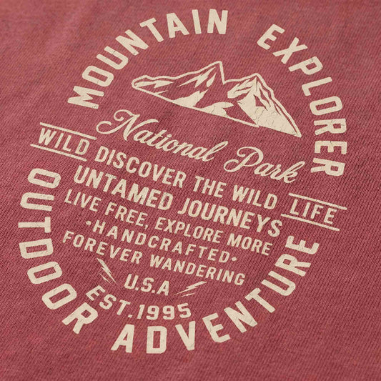 Close-up of a minimal-vintage graphic on a red t-shirt, featuring mountain peaks, trail sign typography, and the text "Mountain Explorer" and "Outdoor Adventure".
