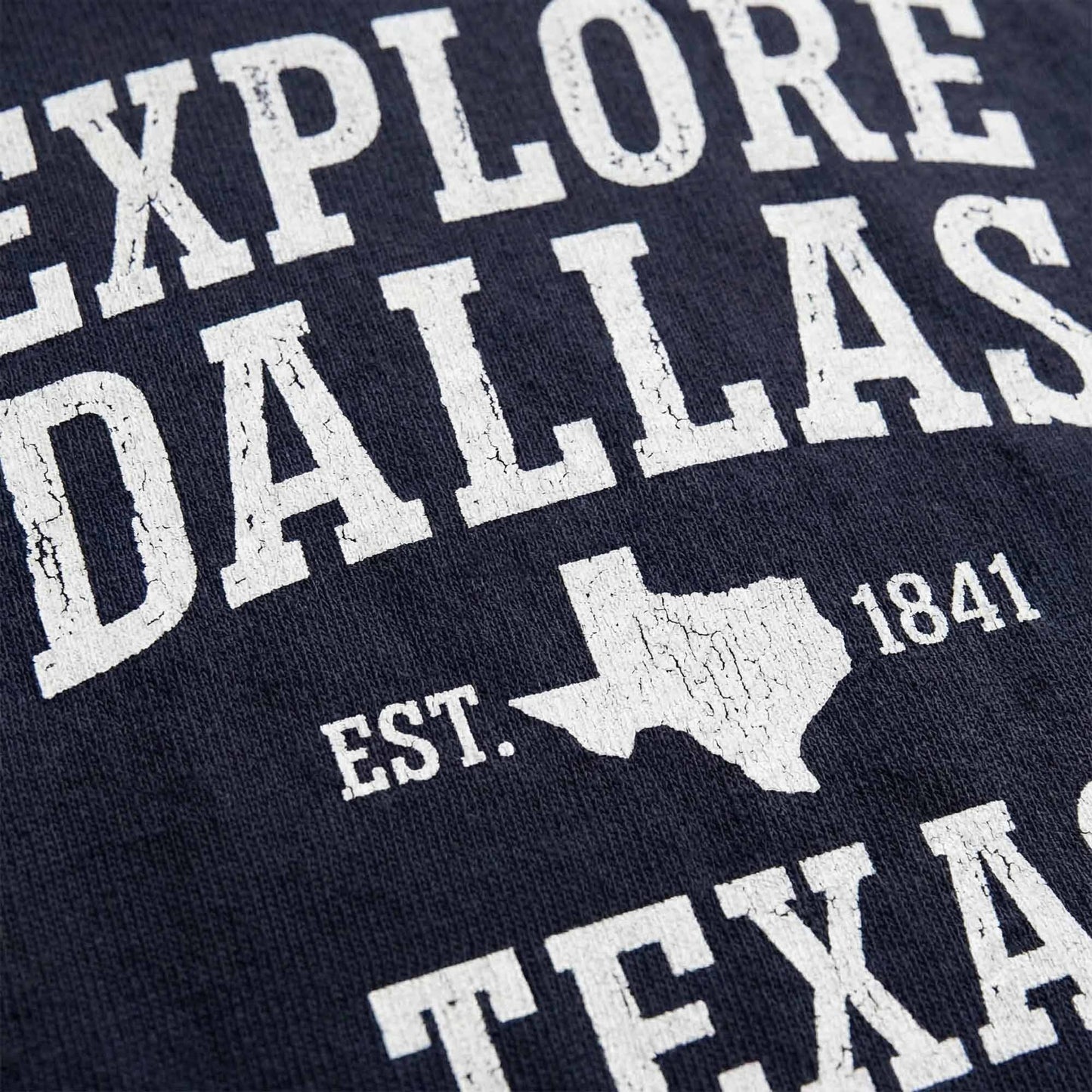 Close-up of vintage distressed Explore Dallas typography graphic on navy t-shirt