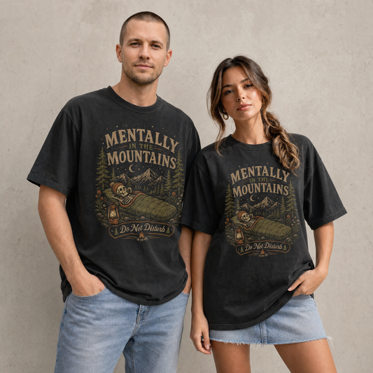 Black vintage outdoor graphic tee featuring a skeleton sleeping in a green sleeping bag under mountain peaks, pine trees, stars, and text reading Mentally in the Mountains Do Not Disturb.