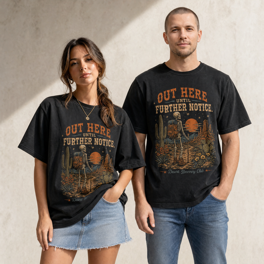 Unisex black graphic tee featuring a skeleton backpacker in a desert sunset scene with cactus, flowers, and “Out Here Until Further Notice” text.
